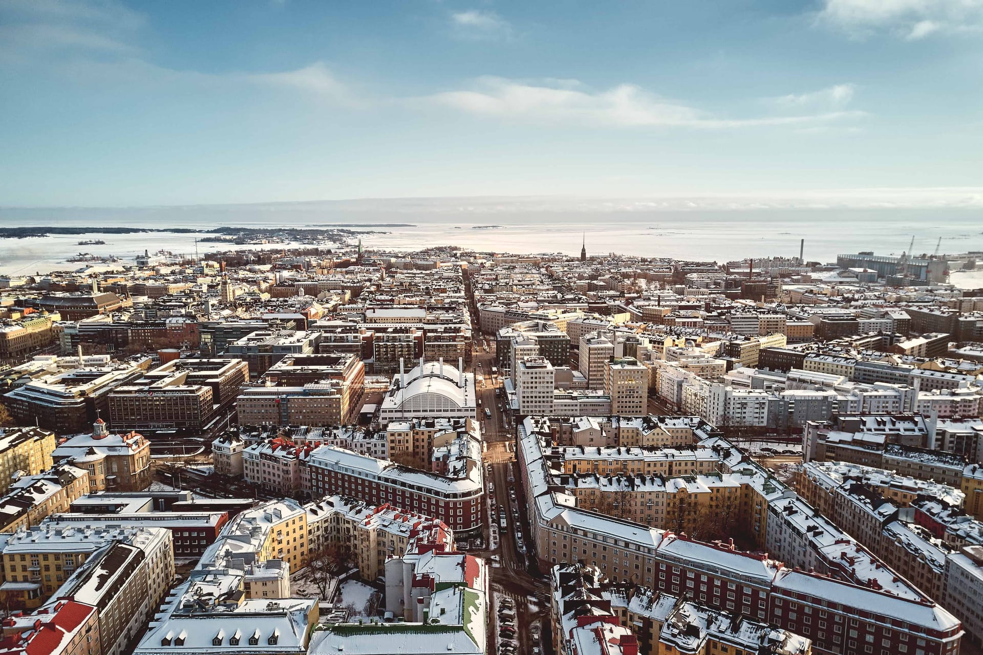 Aerial view of Helsinki in winter, showing snow-covered buildings, city streets and frozen sea under a clear blue sky.