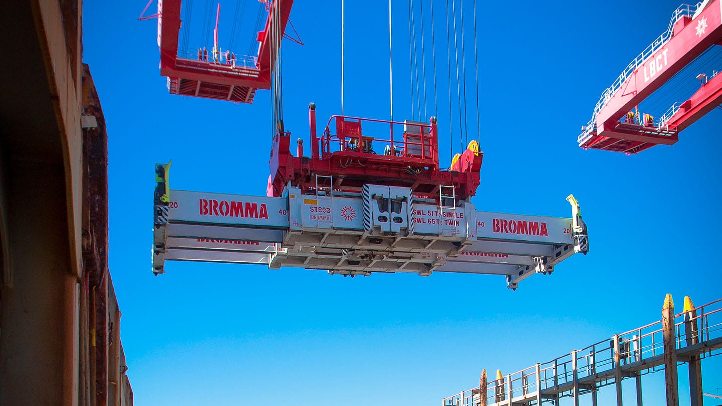 Large Bromma crane lifting equipment suspended in mid-air against bright blue sky at a construction site.
