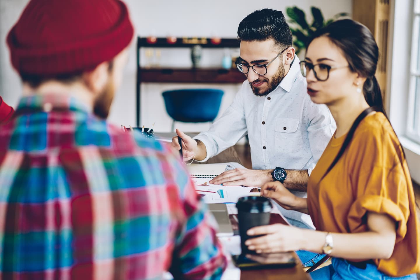 Three young professionals in a meeting, with a person in white shirt explaining something to colleagues wearing colourful attire.