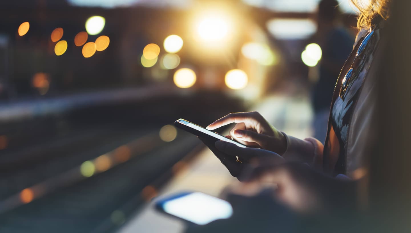 Person using smartphone at night with blurred city lights in background, creating atmospheric urban scene.