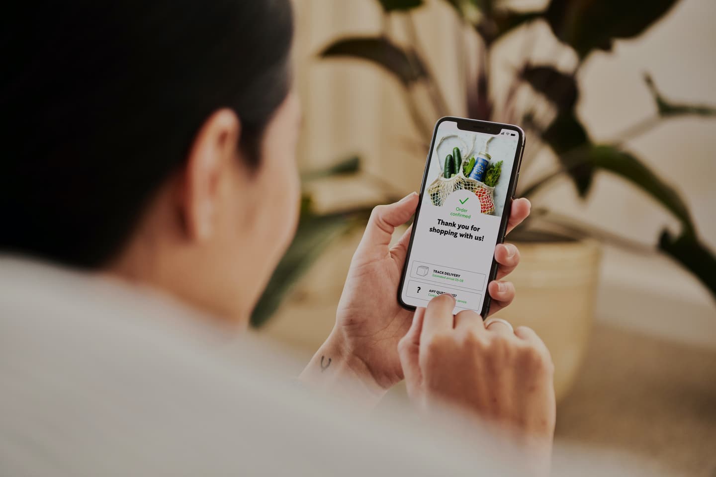 Person using smartphone with grocery delivery app showing order confirmation and mesh bag of vegetables on screen.
