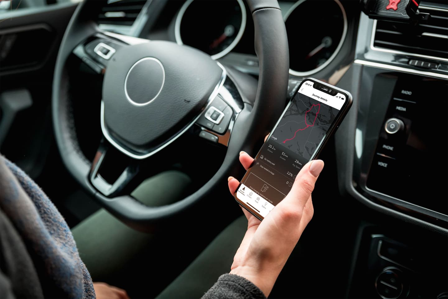 Hand holding smartphone with navigation app showing route map and journey details inside a car with modern dashboard.
