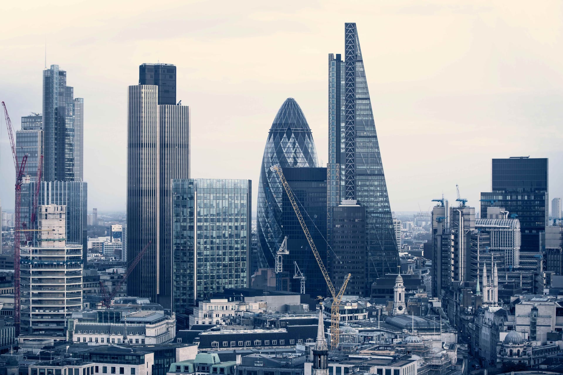 London skyline featuring iconic skyscrapers including the Gherkin and Shard against a pale grey sky.