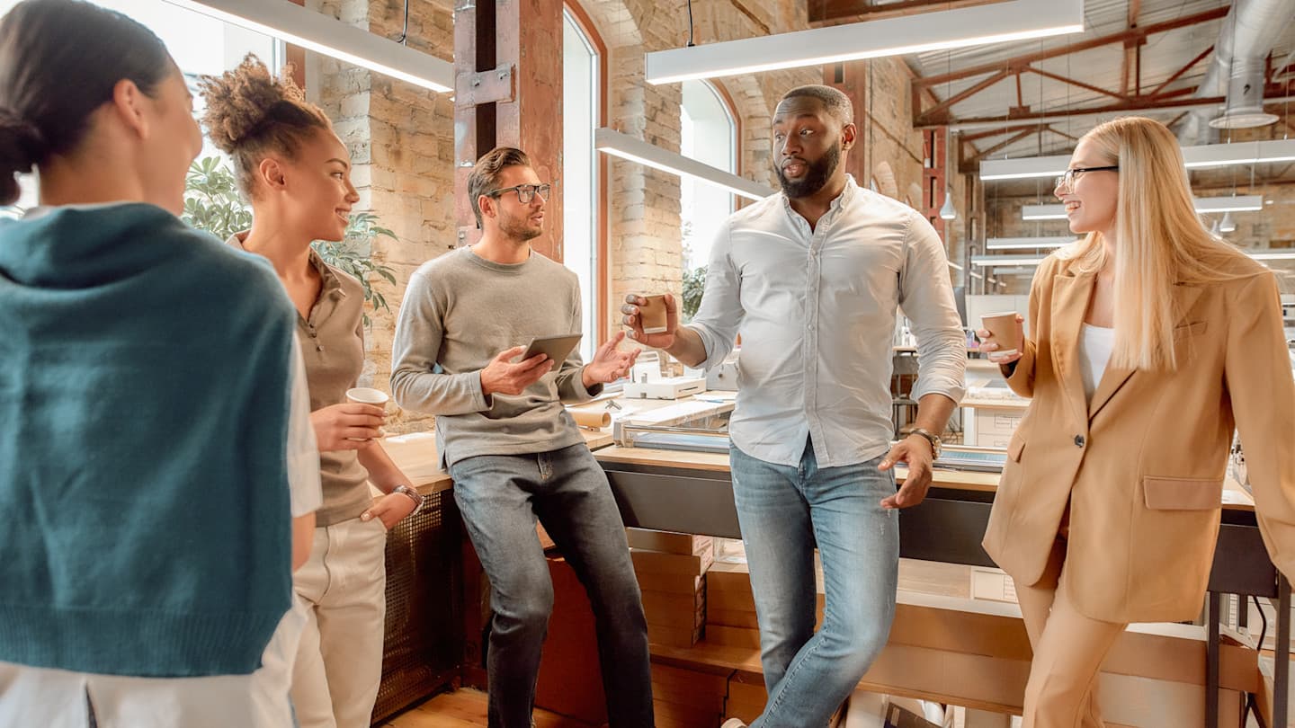 Diverse professionals having a casual meeting in a modern brick office space with coffee cups and natural lighting.