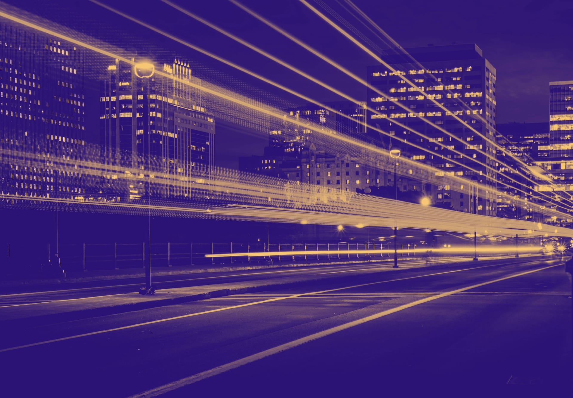 Night cityscape with purple-tinted light trails from traffic against illuminated office buildings in the background.