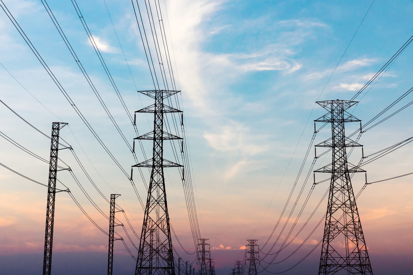 Silhouettes of electrical transmission towers and power lines against a blue and pink sunset sky.
