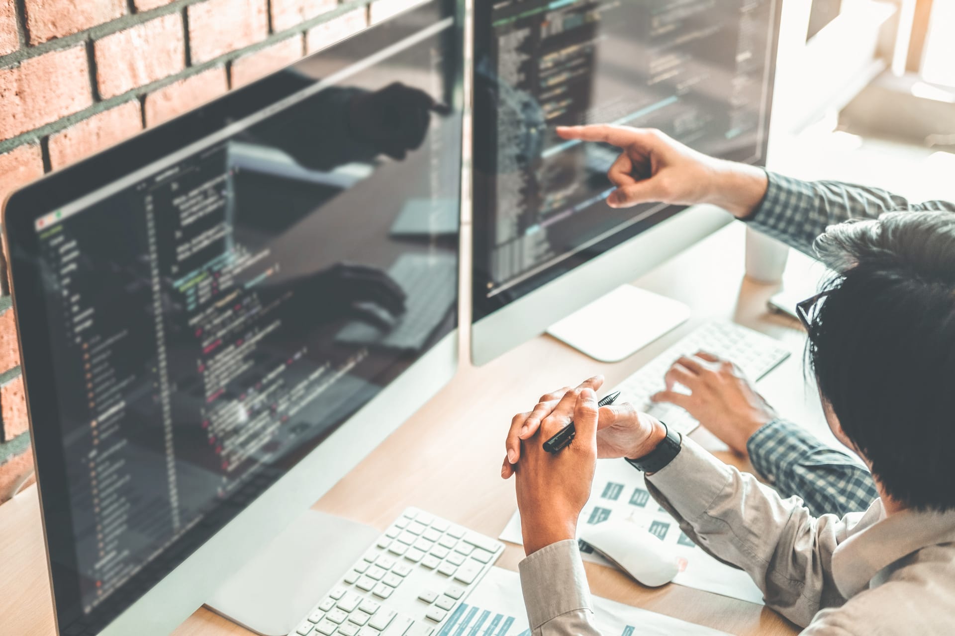 Two persons pointing at monitors and seen in discussion